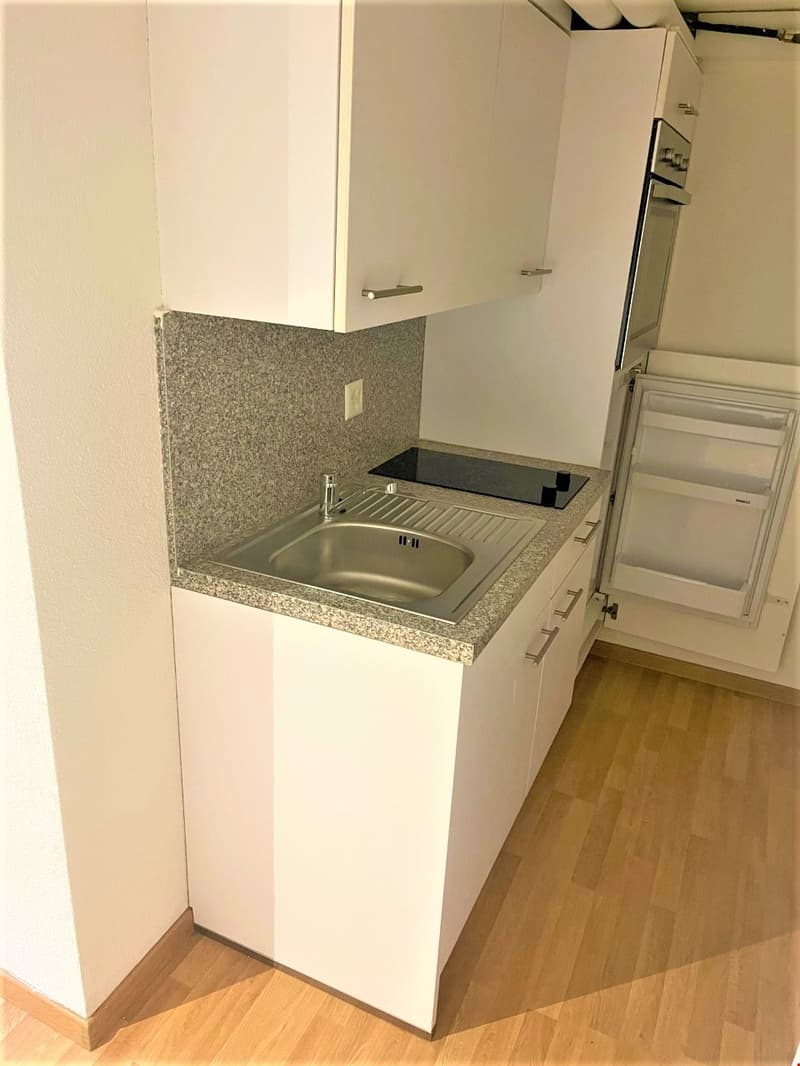 a corner kitchenette, white cabinets, countertop, sink, electrical outlets, stove top, microwave, refrigerator