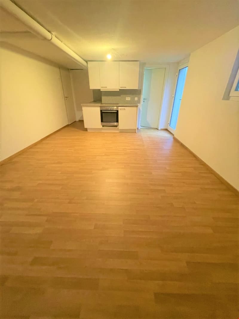 Empty room, kitchen with oven, white cabinets, wooden floor, windows.
