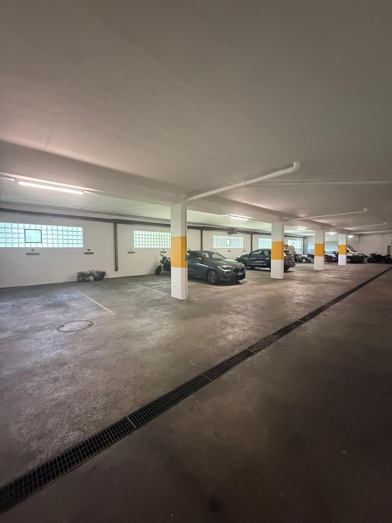 underground parking lot, several cars parked, yellow and white pillars, windows, drain