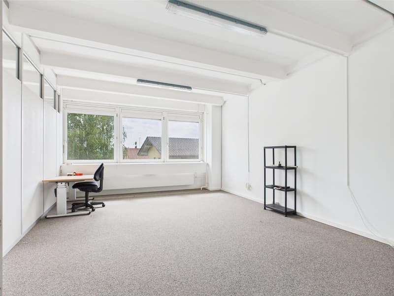 empty room with white walls, gray carpet, office desk with office chair, large window, shelving unit