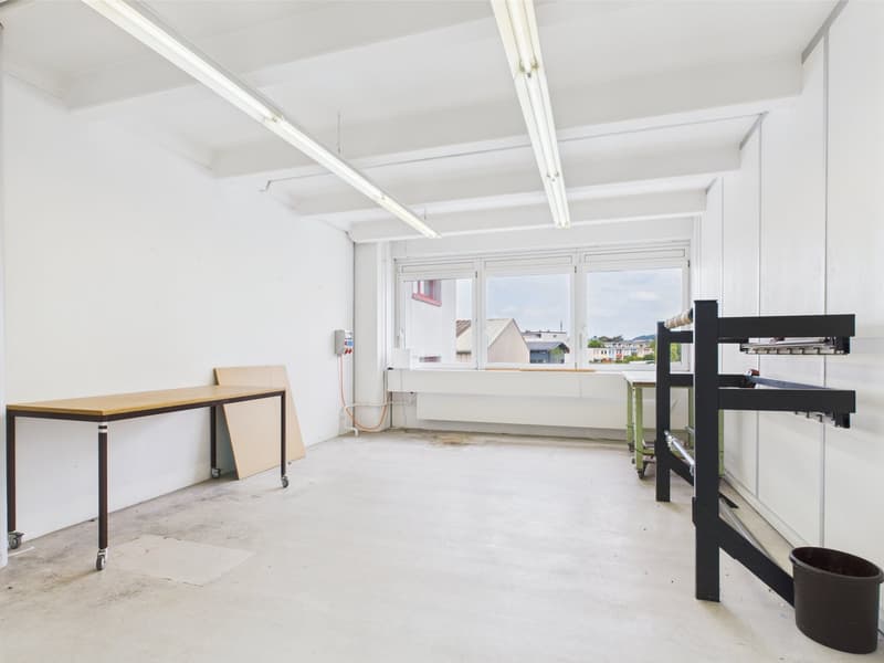 empty room with white walls, wooden table, industrial shelves, white ceiling, and large windows