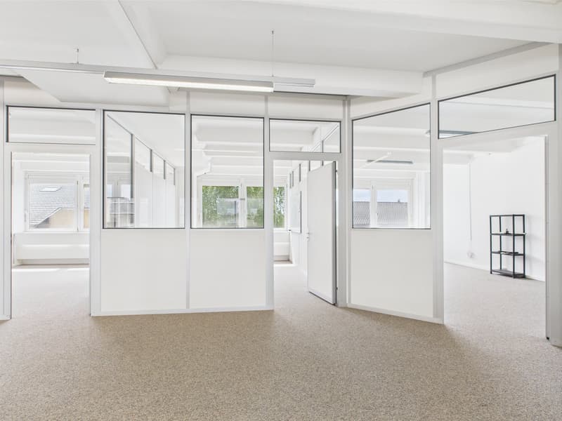 Empty room, white walls, carpet flooring, fluorescent ceiling lights, sliding glass doors, large windows