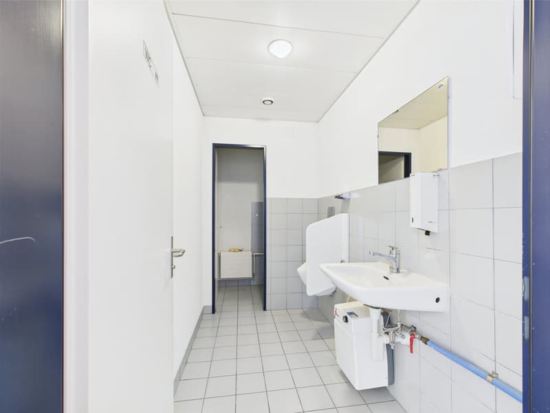 small, empty bathroom with white tiles, modern white sink, toilet, and urinal