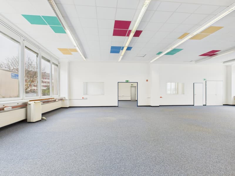 Empty room, white walls, gray carpet, large windows, ceiling lamps, and air conditioning unit.