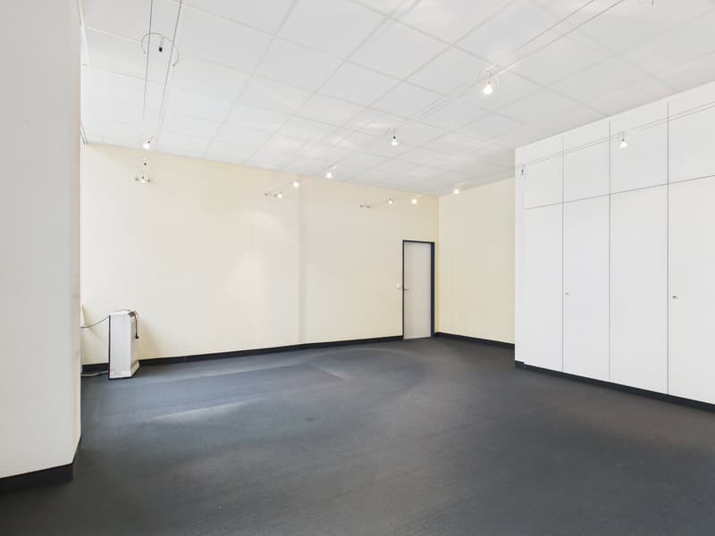 Empty room with white walls and floor, black carpeting, recessed ceiling lights, open door, wall-mounted storage units