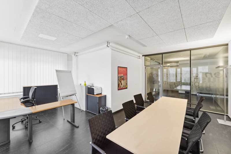 an empty office with desks, chairs, a whiteboard, a printer, a poster, a radiator, a door and windows