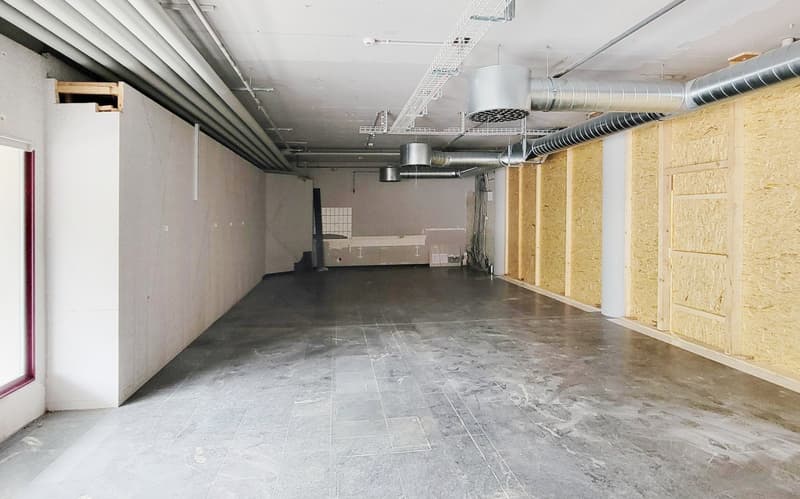 Empty room with pipes on the ceiling, tiles on the floor, and some walls covered in insulation material