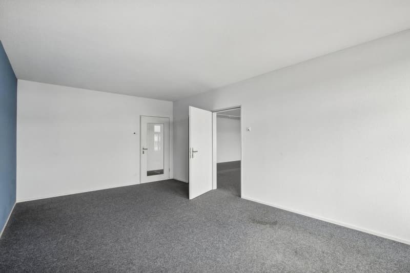 Empty room with white walls, blue accent wall, carpeted floor, two white doors, one open, and an internal door visible.