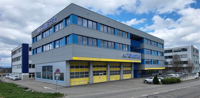 Building: large office building, yellow garage doors, sign says Autometer, cars parked in front