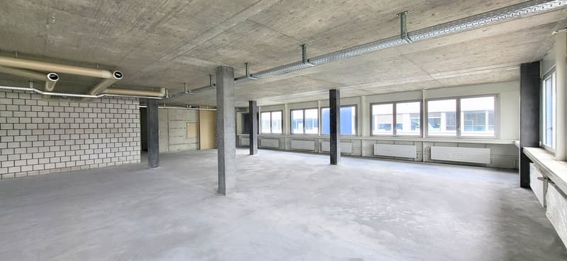 Empty room, exposed concrete columns, brick wall, large windows, central heating