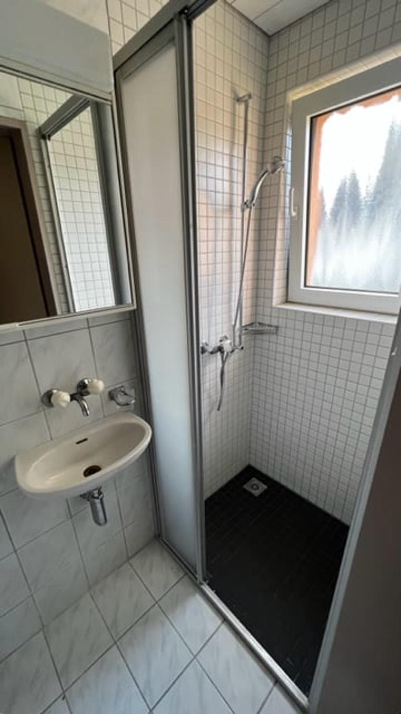 Tiled bathroom with a shower stall, sink, and window overlooking the outdoors.