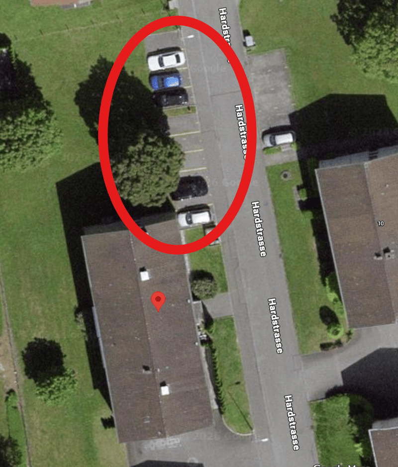 Building with brown roof, circled with a parking area with multiple cars.