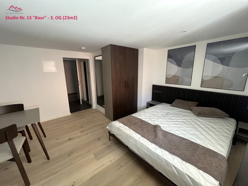 bedroom with bed, bed covers, bed head, nightstands, wardrobe, and paintings on the wall, a small dining table and chairs in the room