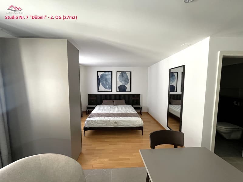 modern interior design, double bed, nightstands, desk, chair, artwork on wall, mirror, entrance to bathroom