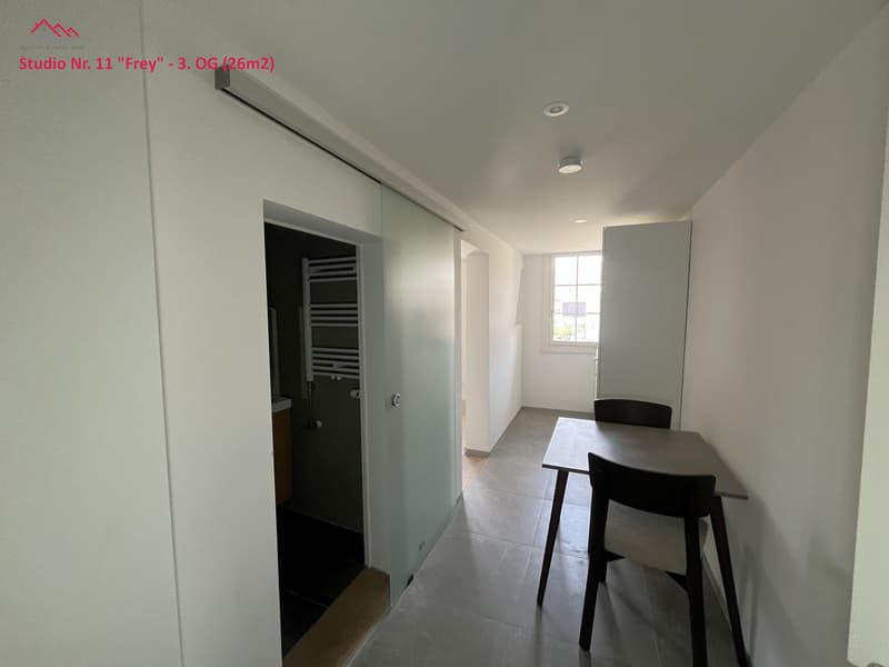 Empty room with modern decor, table, chairs, sliding glass door leading to bathroom