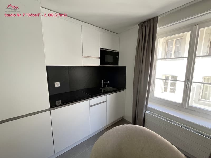 modern kitchen with white cabinetry, black countertops, stainless steel sink, integrated microwave, and a window
