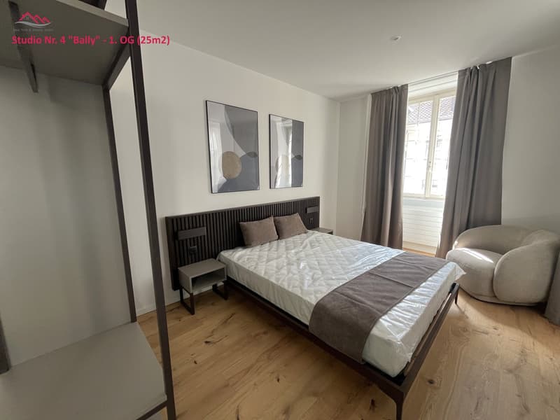 Single bed, night tables, bedhead, two pictures, window with curtains, chair, wooden floor.