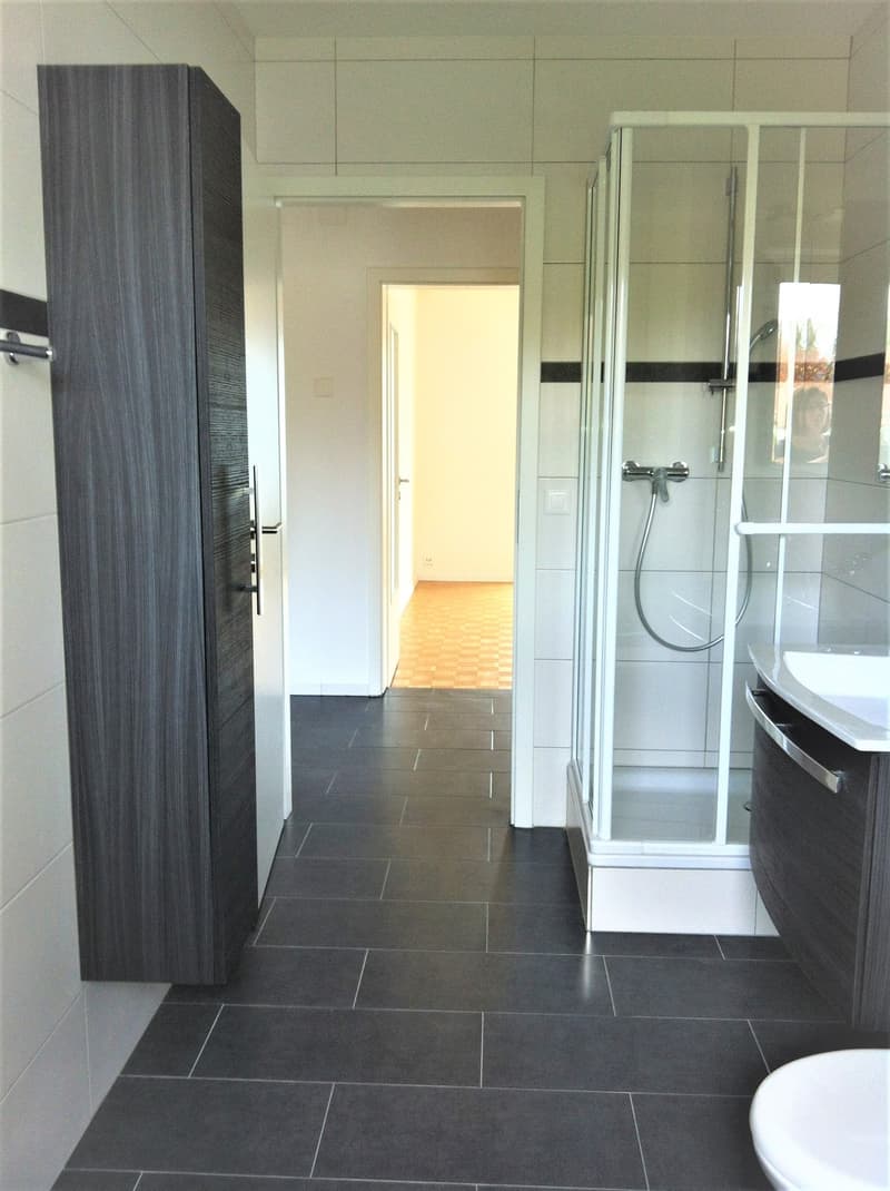modern bathroom with shower, white tiled floor, white vanity, large mirror, toilet
