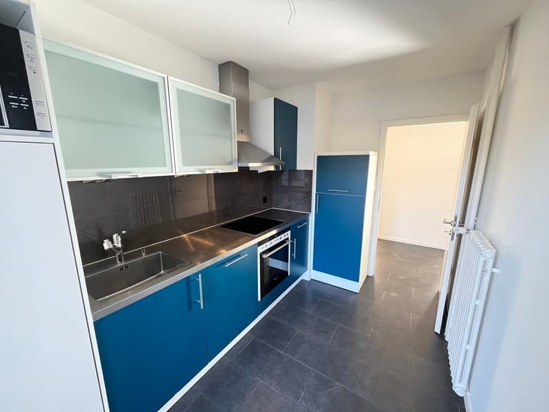 Modern kitchen with blue cabinets, a sink, stove, and microwave on top of the refrigerator, an open door to another room