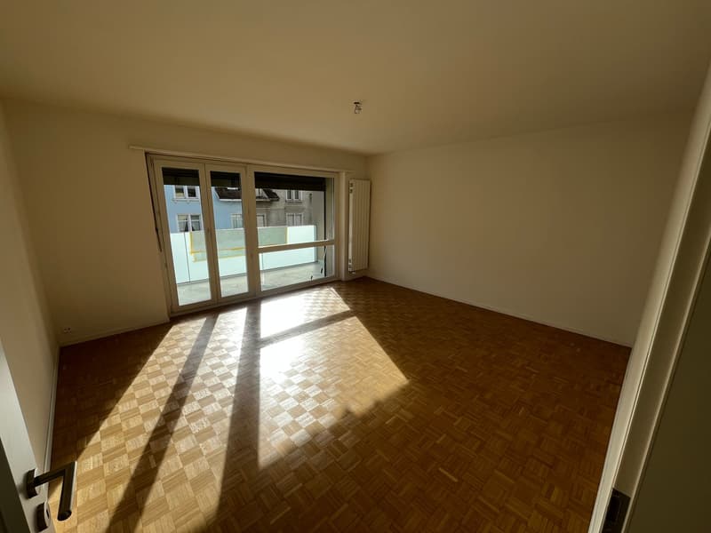 wooden parquet flooring, double sliding glass doors to balcony, white walls, ceiling light, window with curtains