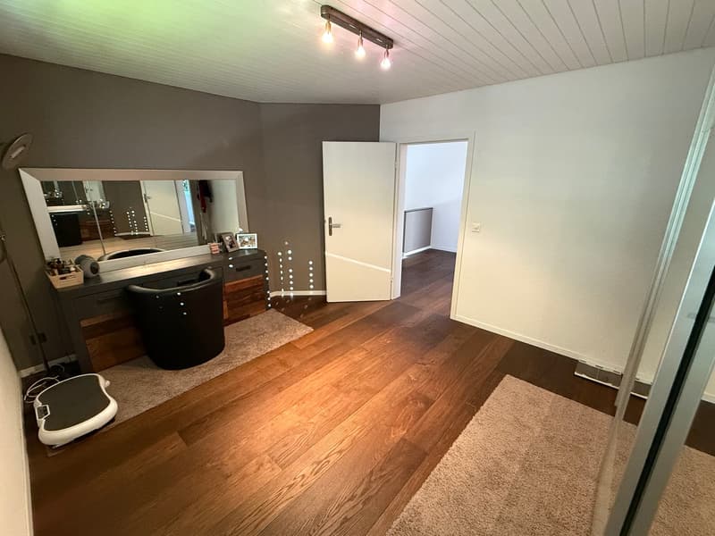 Spacious bedroom with hardwood floors, gray walls, vanity with mirror, and a private washing machine