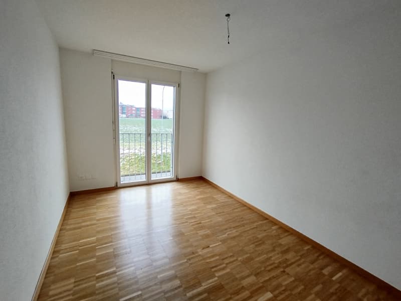 large empty room, white walls, sliding glass door, balcony with metal railings, wooden floor, power outlets on the wall