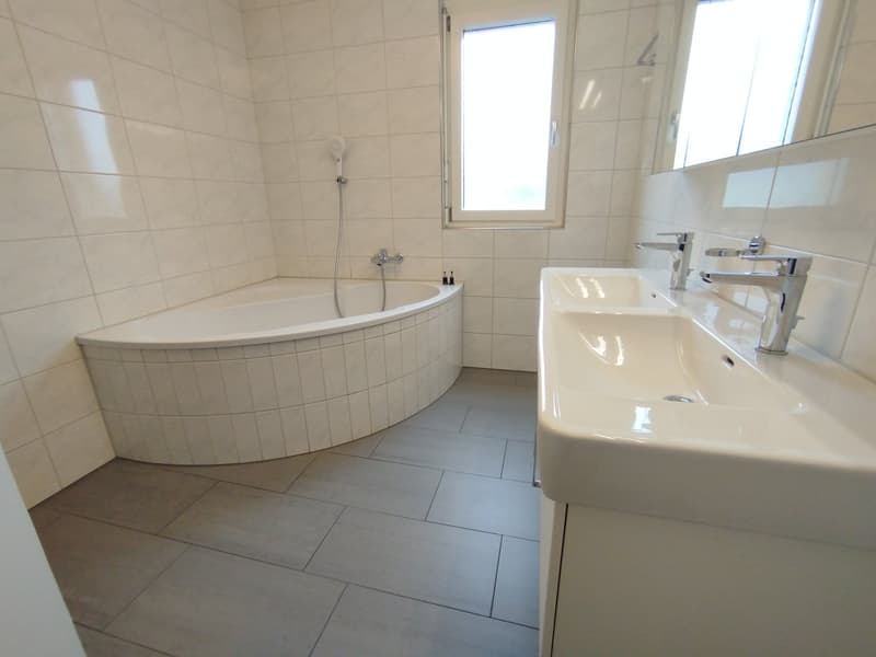 white tiled walls, floor, bathtub, double sink, showerhead, mirrors, grey tiles