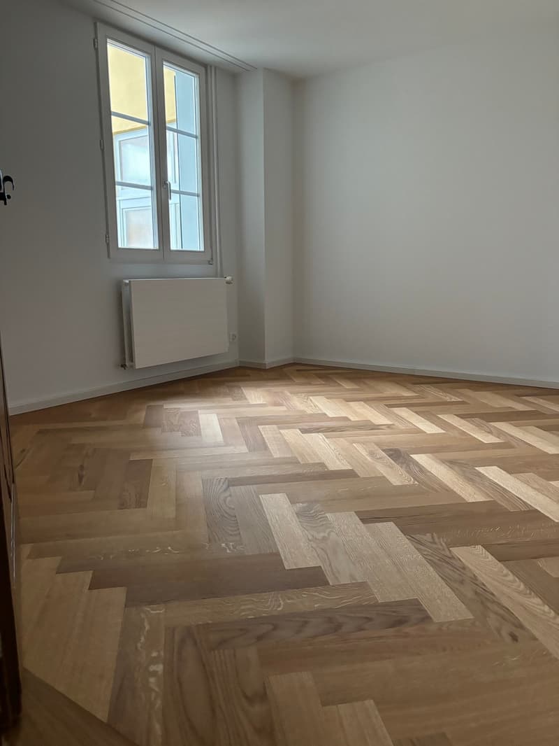 empty room, white walls, parquet flooring, large window, white radiator
