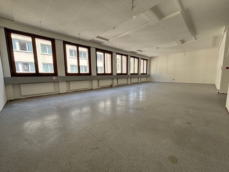 Spacious room, blank walls, white ceiling, gray floor, large windows, electrical outlets