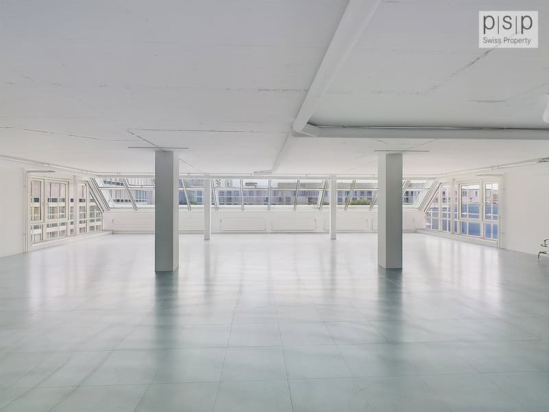 Empty room with high ceiling, tiled floor, multiple large windows with glass balconies, and pillars