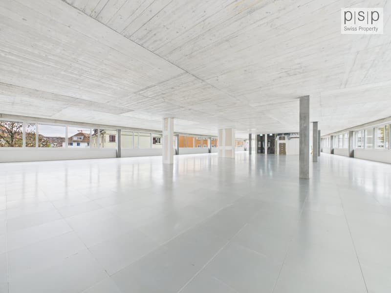 Large empty room, white tiled floor, high ceiling, multiple windows