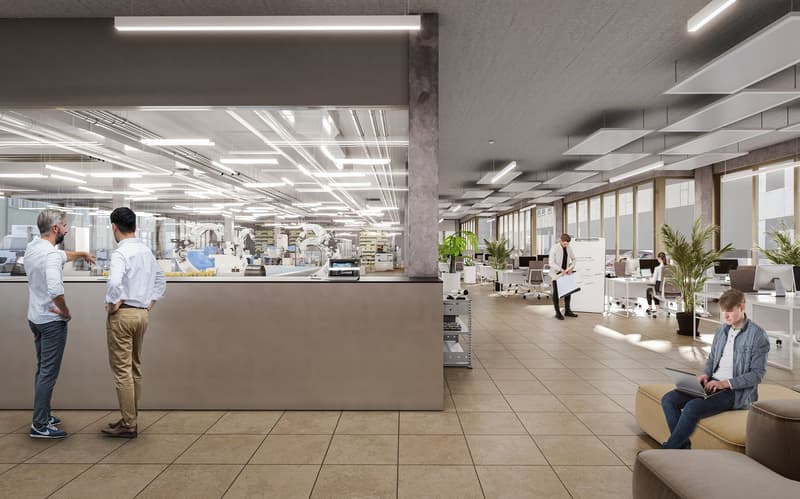 Large open office space with modern design, including suspended lighting fixtures, concrete walls, and tiled flooring. The office has a reception area, workstations, and a visible dishwasher in the background, indicating the presence of a kitchen or break