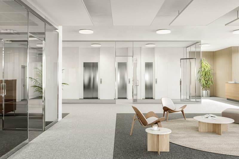 modern office lobby, glass walls, carpeted floor, two elevators, wooden chairs, round coffee table, side tables, large rug