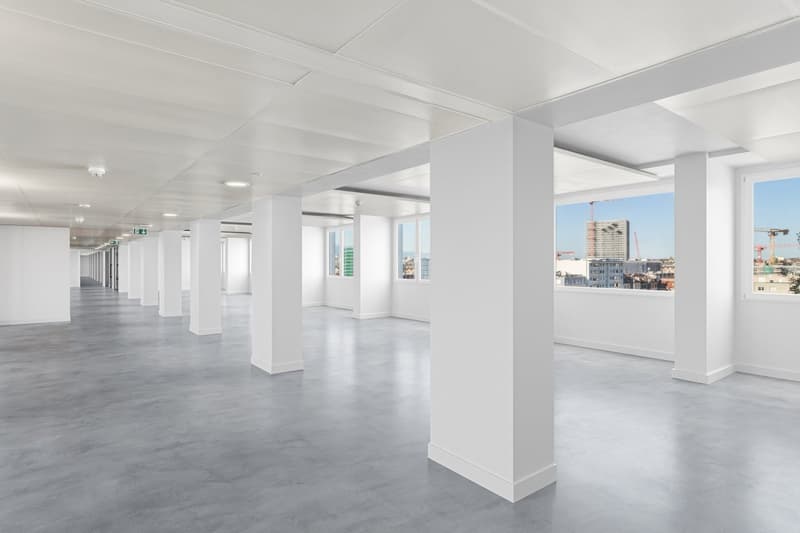 Empty hallway with white walls, gray floor, large windows, and ceiling lights