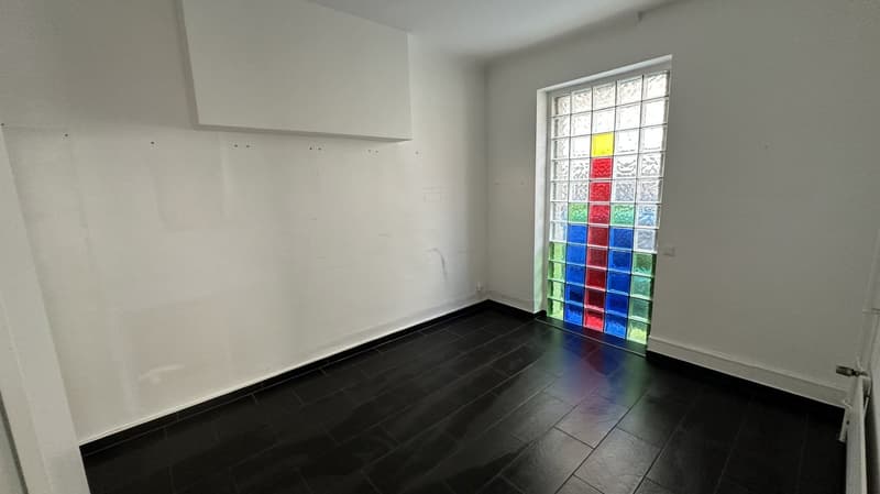 square room with black floor tiles, white walls, large colored glass window, white door on the right