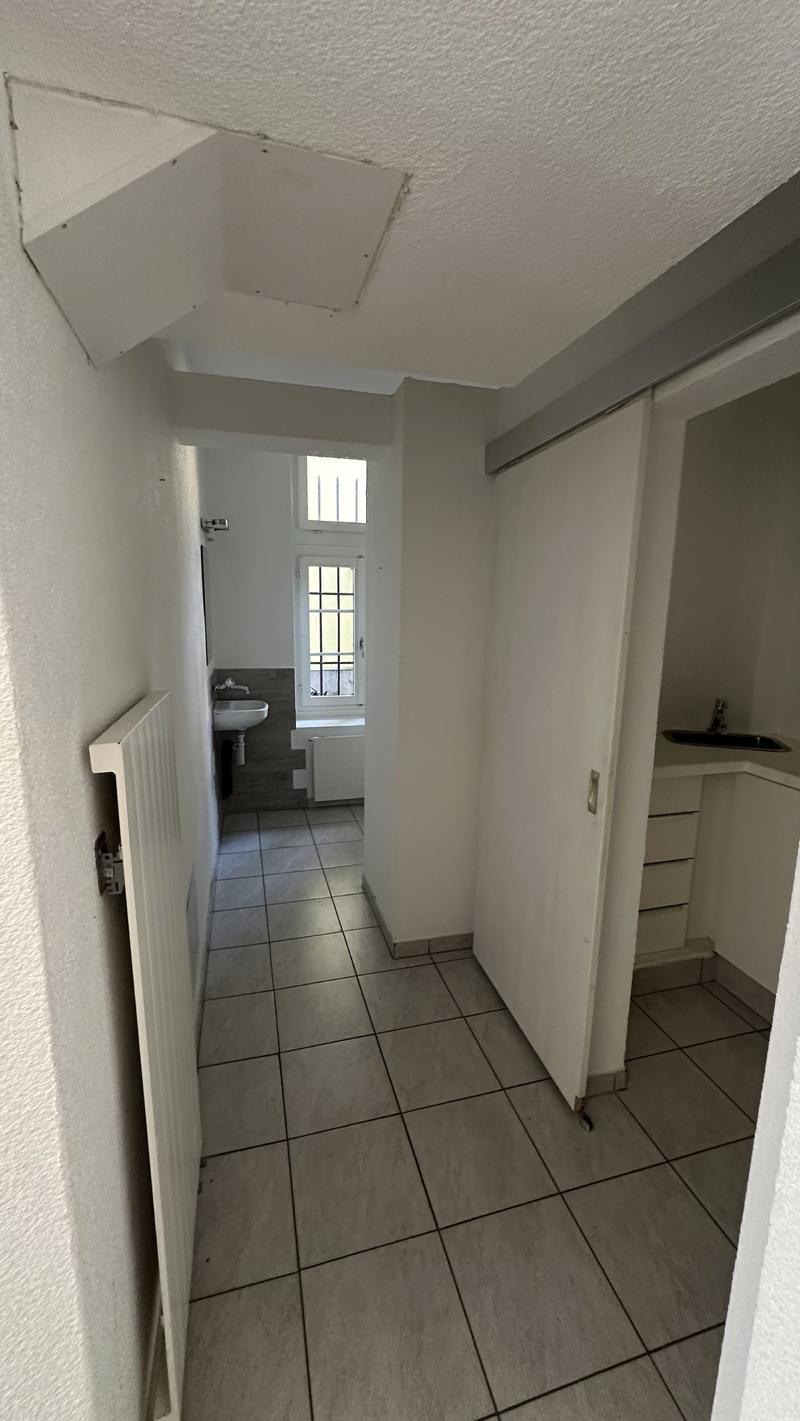 Bathroom with sink, shower, and small toilet, hallway with tiled floor