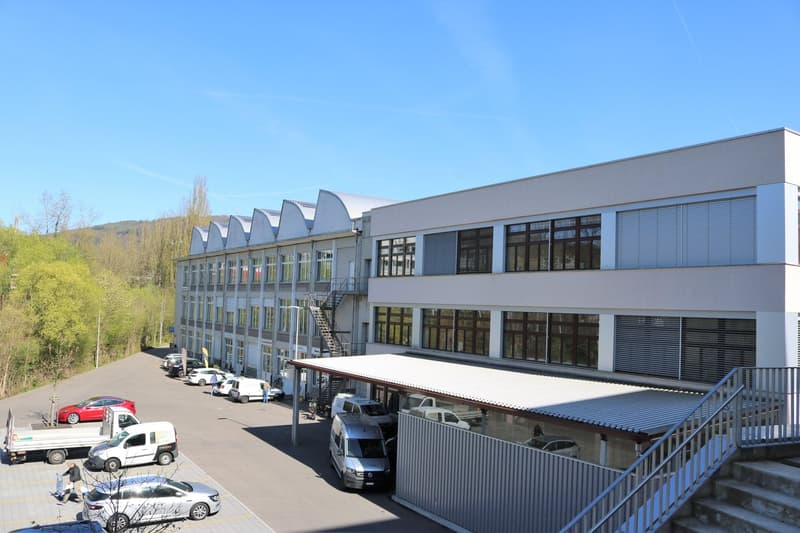 Large industrial building with multiple stories and extensive parking area in front.