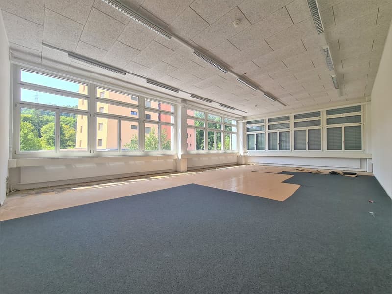 Large room with glass windows, gray carpet, modern lighting, construction materials on the floor