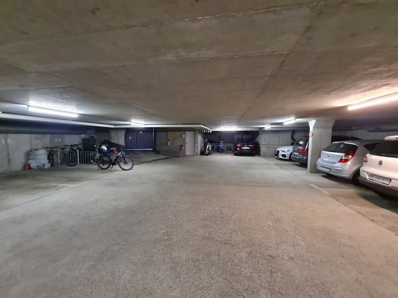 underground parking garage, several cars parked, storage areas, bike racks