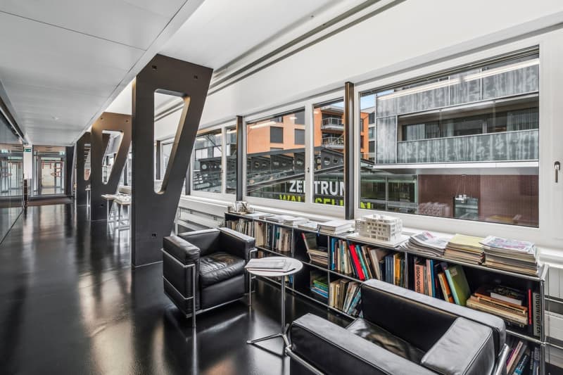 Large open office space with high ceilings, large windows, black leather chairs, bookshelves, and modern architectural elements
