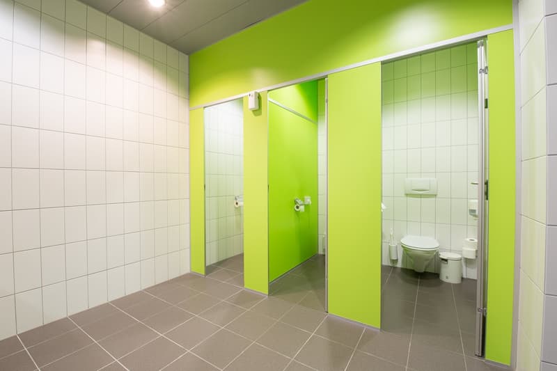 Large bathroom with bright green walls, white tiled walls, gray tile flooring, toilet, and glass shower stalls