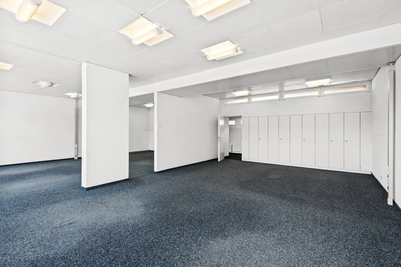 Empty room with white walls, white ceiling, dark blue carpet, recessed lighting, white cabinets, door