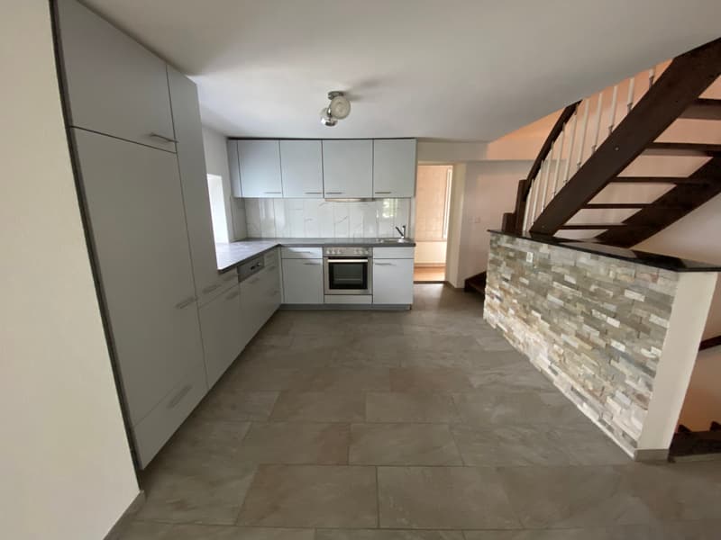 Modern kitchen with grey cabinets, built-in oven, tiled floor, and exposed wooden beams