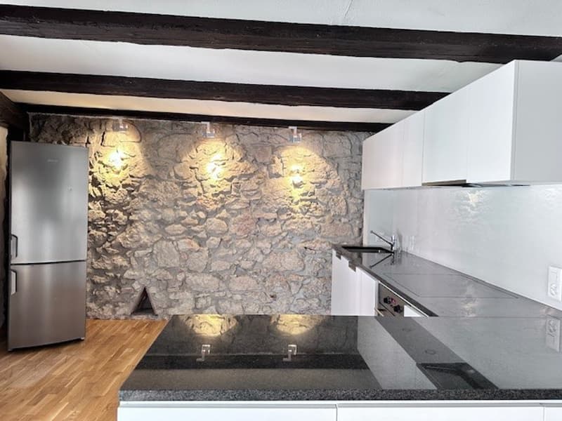 kitchen with stone wall, stainless steel refrigerator, white cabinets, marble countertop, and silver sink and faucet