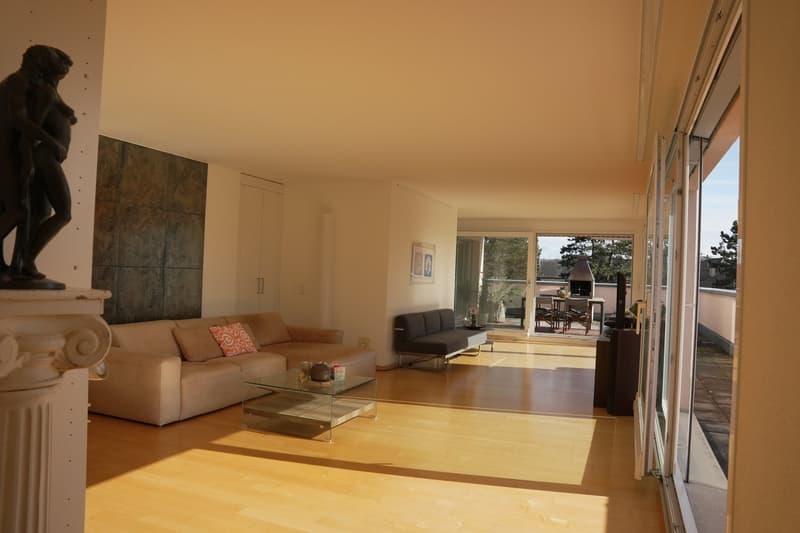 Spacious living room with hardwood floors, large windows, a beige sofa, a glass coffee table, and a balcony or terrace visible through the sliding glass doors.