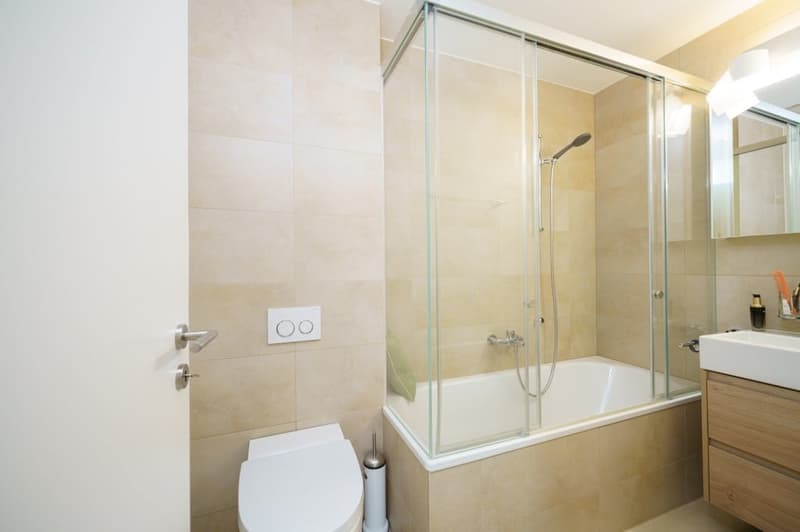 modern bathroom with bathtub, shower, toilet, sink, and wooden cabinet