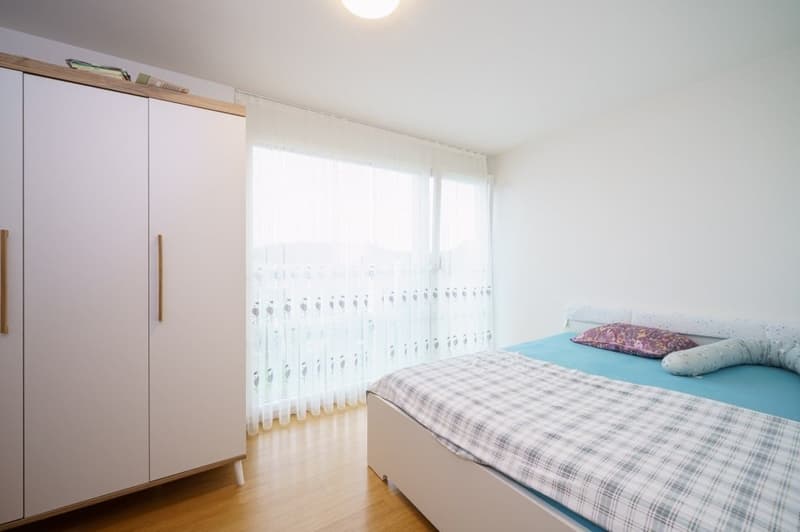 Bedroom with bed, white wardrobe, wooden floor, large window with curtains, ceiling lamp