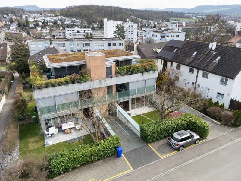 Modern house with green roof, glass balcony, solar panels, car parked in front