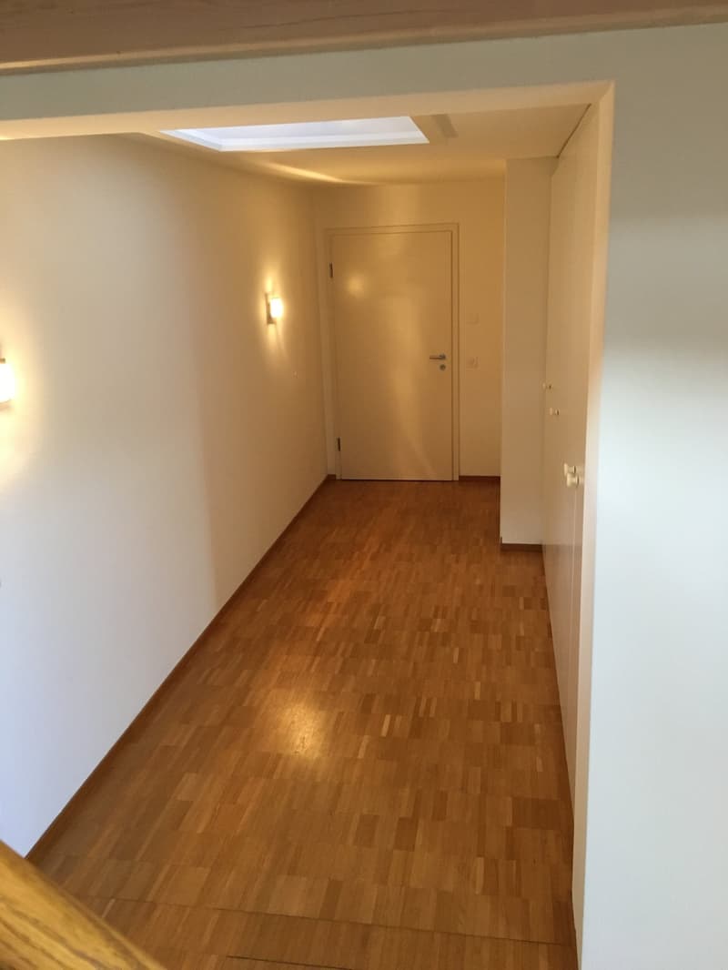 Empty room with wooden floor, white walls, white door, and two wall lights