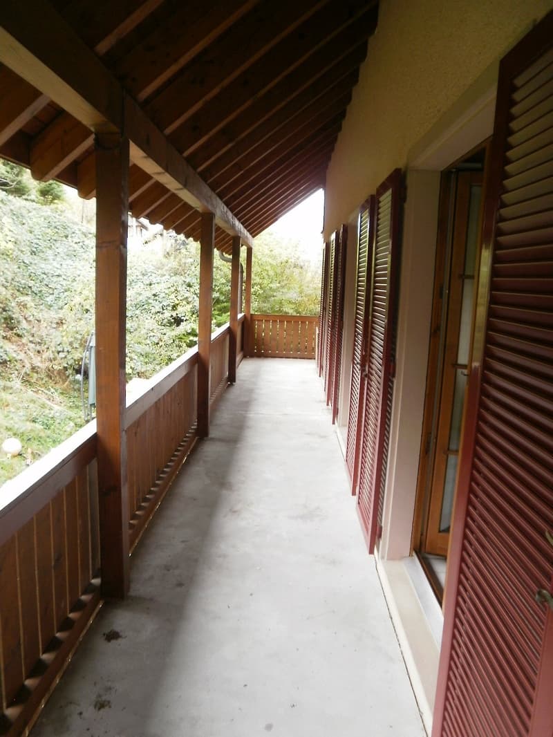 balcony with wooden railings, concrete floor, red shutters, wooden ceiling